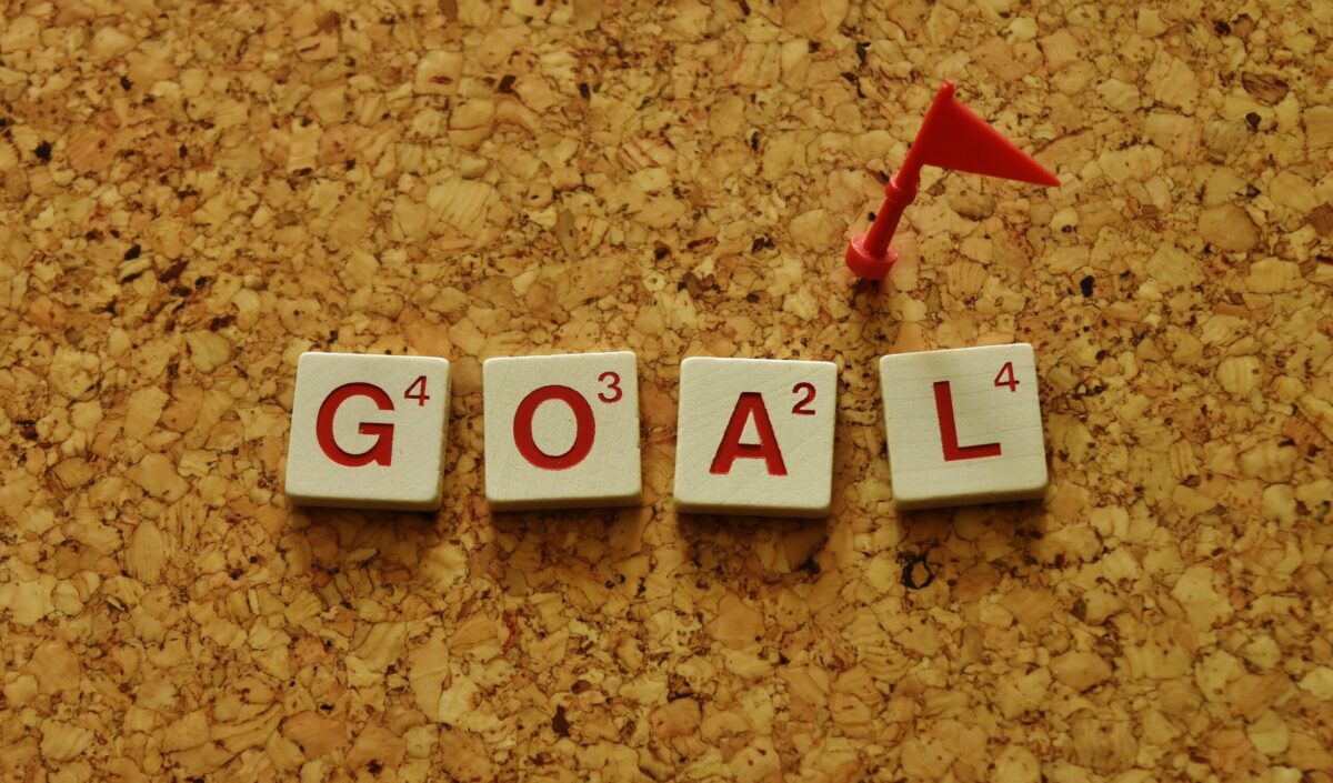 コルクボードの上に並んだ“GOAL”の文字タイルと赤い旗。目標設定や達成を象徴する写真。