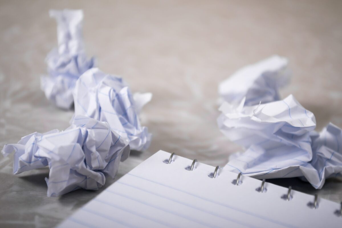 書き直しを重ねる様子を表す、くしゃくしゃの紙とノート。くやしさをイメージ。